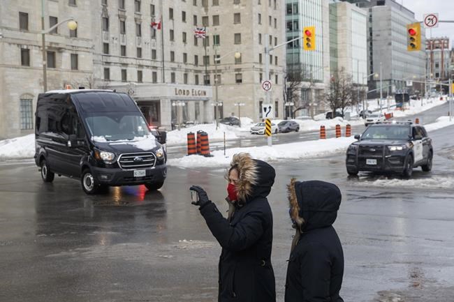 People walk by and film as police work checkpoints in downtown in Ottawa on Monday, Feb. 21, 2022, after officers cleared a trucker protest that was aimed at COVID-19 measures before growing into a broader anti-government protest that occupied the nation capital’s downtown core. THE CANADIAN PRESS/Cole Burston