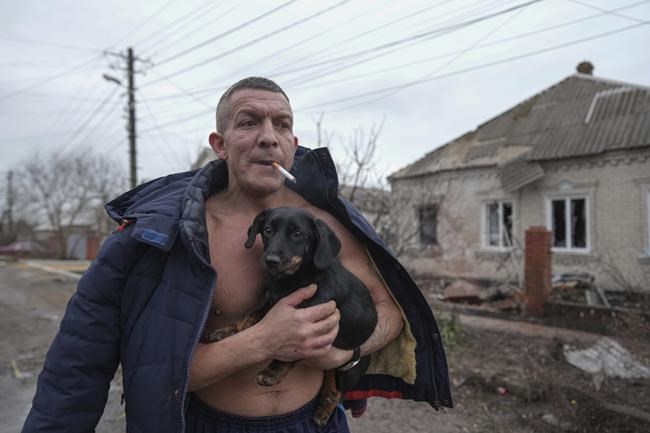 A man holds a dog as he walks past a damaged house following Russian shelling, in Mariupol, Ukraine, Thursday, Feb. 24, 2022. Russia launched a wide-ranging attack on Ukraine on Thursday, hitting cities and bases with airstrikes or shelling, as civilians piled into trains and cars to flee. (AP Photo/Evgeniy Maloletka)