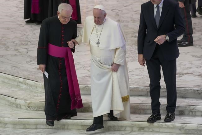 FILE - Pope Francis, center, holds onto Monsignor Leonardo Sapienza as he walks down some steps during his weekly general audience in the Paul VI Hall at the Vatican, on Feb. 09, 2022. Pope Francis has canceled a visit Sunday to Florence and will not preside over Ash Wednesday commemorations next week because of what the Vatican said Friday was a flareup of “acute” knee pain. The Vatican said the 85-year-old pope was cancelling his participation after his doctors prescribed a period of rest. The pope has been suffering for several weeks for what he has said is an inflamed ligament in his right knee. (AP Photo/Gregorio Borgia)