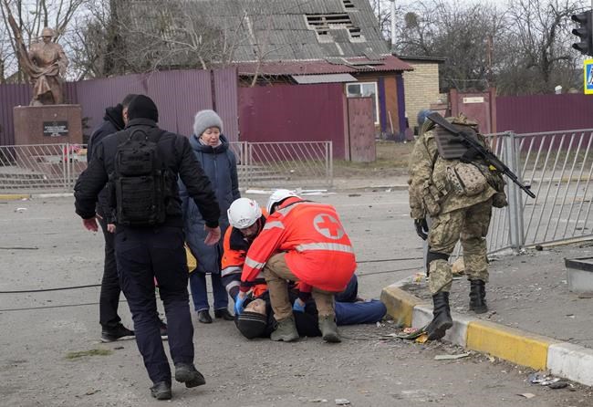 Paramedics administer first aid to an elderly man who fainted after crossing the Irpin river to flee the town of Irpin, close to Kyiv, Ukraine, Monday, March 7, 2022. Irpin residents continue to leave the ruined city under Russian heavy artillery shelling. (AP Photo/Efrem Lukatsky)