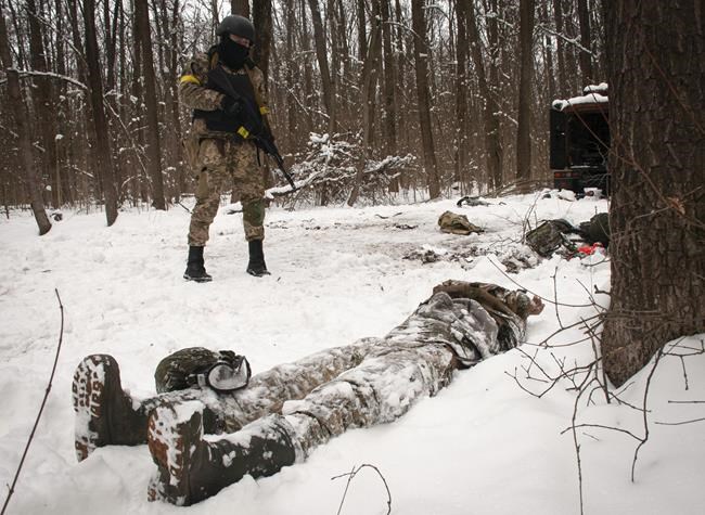 A volunteer of the Ukrainian Territorial Defense Forces looks at a dead body of a soldier lying in a forest in the outskirts of Kharkiv, Ukraine's second-largest city, Monday, March 7, 2022. Russia announced yet another cease-fire and a handful of humanitarian corridors to allow civilians to flee Ukraine. Previous such measures have fallen apart and Moscow’s armed forces continued to pummel some Ukrainian cities with rockets Monday. (AP Photo/Andrew Marienko).