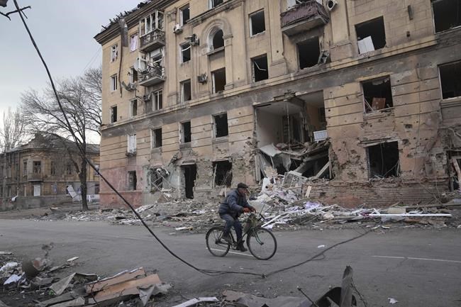 A man rides a bicycle in front of a damaged by shelling apartment building in Mariupol, Ukraine, Wednesday, March 9, 2022. A Russian attack has severely damaged a maternity hospital in the besieged port city of Mariupol, Ukrainian officials say. (AP Photo/Evgeniy Maloletka)
