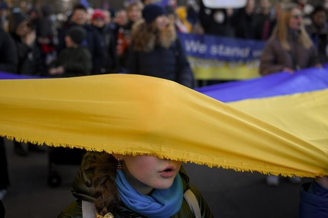 A child with her face covered by a large Ukrainian flag sings the Ukrainian national anthem during a protest against Russia's war in Ukraine, in Bucharest, Romania, Saturday, March 19, 2022. (AP Photo/Andreea Alexandru)