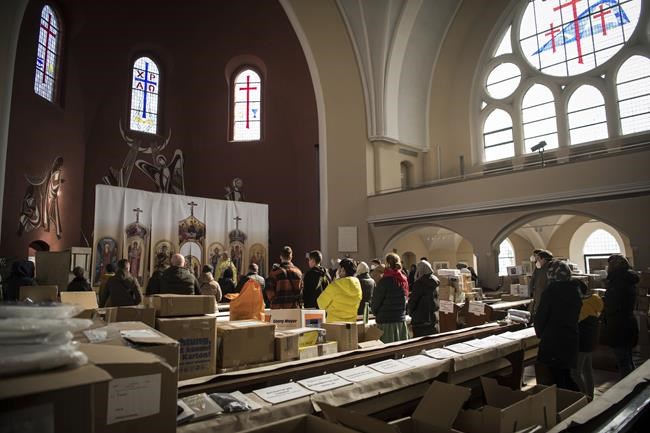 Members of the Ukrainian Orthodox community, who have found shelter for their church service in an evangelical church, and refugees from Ukraine celebrate a church service and pray for peace between boxes with collected aid supplies in Berlin, Sunday, March 20, 2022. (AP Photo/Steffi Loos)