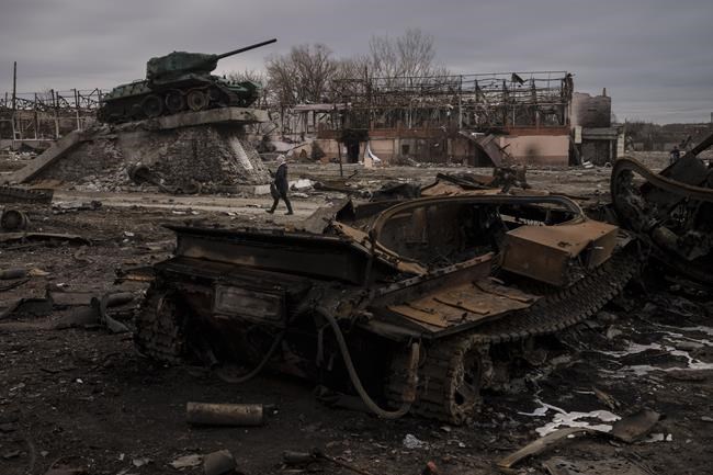 A woman walks past a destroyed tank in the town of Trostsyanets, Ukraine, Monday, March 28, 2022. Trostsyanets was recently retaken by Ukrainian forces after being held by Russians since the early days of the war. (AP Photo/Felipe Dana)