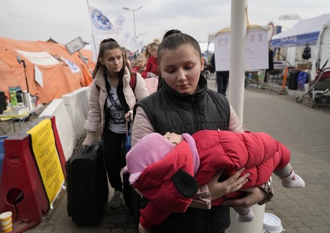 A refugee carries a baby after fleeing the war from neighbouring Ukraine at the border crossing in Medyka, southeastern Poland, on Tuesday, March 29, 2022. The daily number of people fleeing Ukraine has fallen in recent days but border guards, aid agencies and refugees say Russia's unpredictable war offers few signs whether it's just a temporary lull or a permanent drop-off. (AP Photo/Sergei Grits)