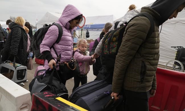 People carry their belongings after fleeing the war from neighbouring Ukraine at the border crossing in Medyka, southeastern Poland, on Tuesday, March 29, 2022. The daily number of people fleeing Ukraine has fallen in recent days but border guards, aid agencies and refugees say Russia's unpredictable war offers few signs whether it's just a temporary lull or a permanent drop-off. (AP Photo/Sergei Grits)