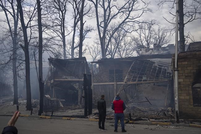 Men look at their restaurant set on fire by people who previously looted it in Bucha, in the outskirts of Kyiv, Ukraine, Monday, April 11, 2022. (AP Photo/Rodrigo Abd)