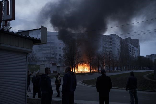 Residents stand outside their apartments as shops burn after a Russian attack in Kharkiv, Ukraine, Monday, April 11, 2022. (AP Photo/Felipe Dana)