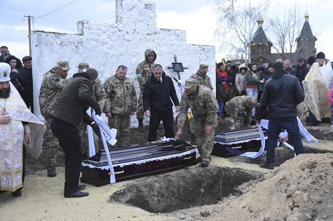 Ukrainian servicemen prepare to lower coffins of their comrades Yuri Filyuk, 49, and Oleksander Tkachenko, 33, in a village of Oleksandrivka, Odesa region, Ukraine, Tuesday, April 12, 2022. According to Ukrainian servicemen, these two were killed by a Russian missile hit their military base in Krasnoselka, Odesa region, on April 7. (AP Photo/Max Pshybyshevsky)