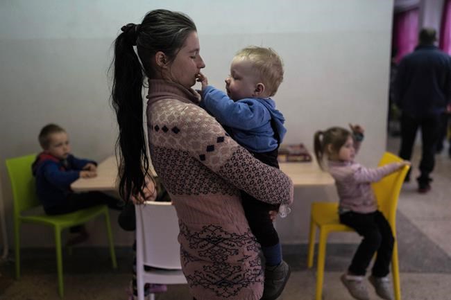 Marta Fedorova holds her baby boy as her son Volodymir 6, and her daughter Violetta 5, right, sit inside a school that is being used as a shelter for people who fled the war, in Dnipro city, Ukraine, on Tuesday, April 12, 2022. Marta Fedorova with her husband and five children fled from the city of Bahmud. (AP Photo/Petros Giannakouris)