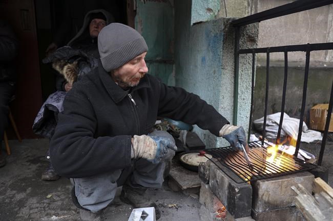 A local resident prepares to cook at an entrance of the building damaged during fighting in Mariupol, on the territory which is now under the Government of the Donetsk People's Republic control, eastern in Mariupol, Ukraine, Wednesday, April 13, 2022. (AP Photo/Alexei Alexandrov)