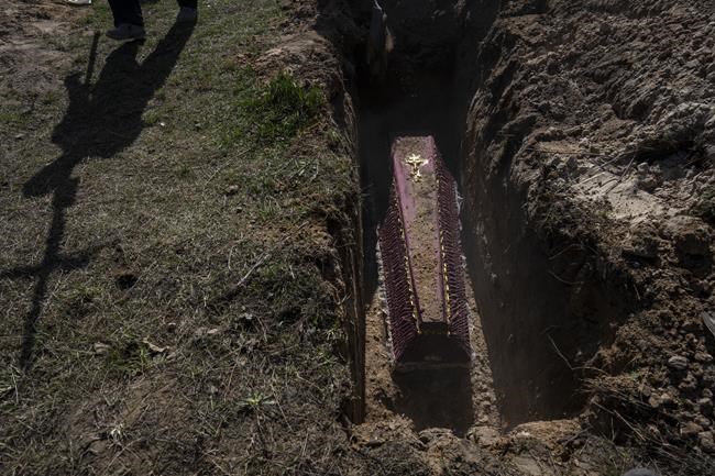 A cemetery worker carries a cross for the tomb of Tetyana Gramushnyak, 75, who was killed by shelling on March 19 while cooking food outside her home in Bucha, on the outskirts of Kyiv, Ukraine, Thursday April 14, 2022. (AP Photo/Rodrigo Abd)