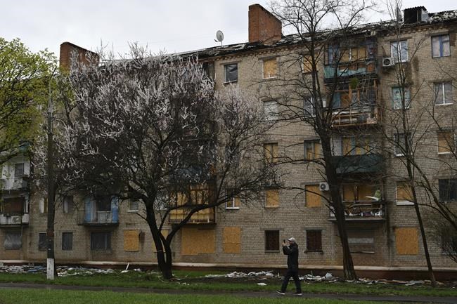 A man takes photos and walks past an apartment building with windows covered by plywood due to shelling in Kramatorsk, Ukraine, Thursday, April 14, 2022. (AP Photo/Andriy Andriyenko)