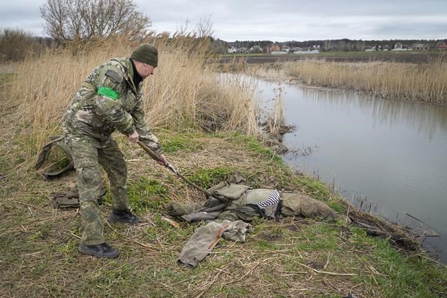 An interior ministry sapper checks the body of a Russian soldier as he searches for unexploded devices, in the village of Moshchun, close to Kyiv, Ukraine, Tuesday, April 19, 2022. (AP Photo/Efrem Lukatsky)
