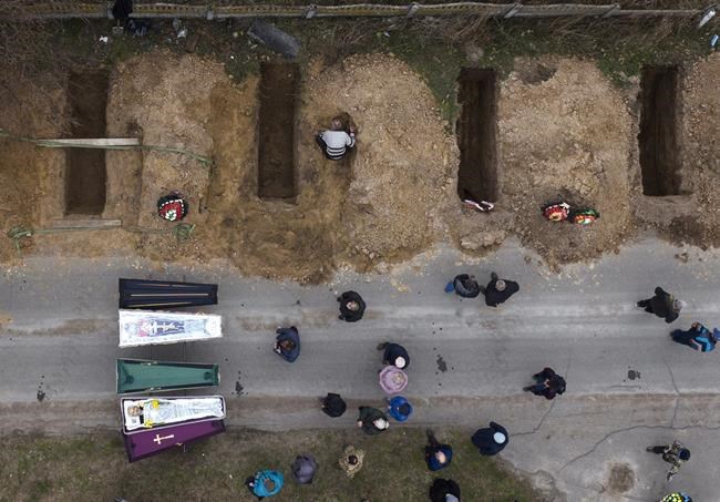 The bodies of four people who died during the Russian occupation await burial during funerals in Bucha, on the outskirts of Kyiv, Wednesday, April 20, 2022. (AP Photo/Emilio Morenatti)