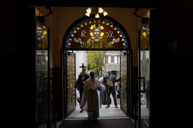 Fr. Mykola Ivanov enters the front doors of Transfiguration of Our Lord Ukrainian Catholic Church in Shamokin, Pa., Sunday, April 17, 2022, during Easter Morning Devine Services to symbolize the opening the tomb of Jesus. Joshua Wisotski is left and Dave Kaleta is right. (AP Photo/Carolyn Kaster)