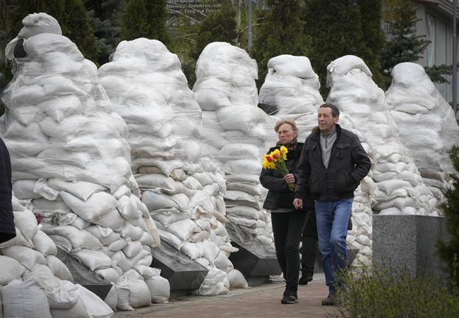 People pay respect to the Chernobyl firefighters at a memorial in capital Kyiv, Ukraine, Tuesday, April 26, 2022. At left, firefighter sculptures are covered with bags to protect against the Russian shelling. April 26 marks the 36th anniversary of the Chernobyl nuclear disaster. A reactor at the Chernobyl nuclear power plant exploded on April 26, 1986, leading to an explosion and the subsequent fire spewed a radioactive plume over much of northern Europe. (AP Photo/Efrem Lukatsky)