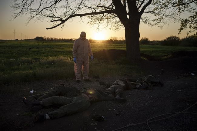 A Ukrainian emergency worker stands next to the bodies of Russian soldiers in the village of Vilkhivka, recently retaken by Ukrainian forces near Kharkiv, Ukraine, Monday, May 9, 2022. (AP Photo/Felipe Dana)