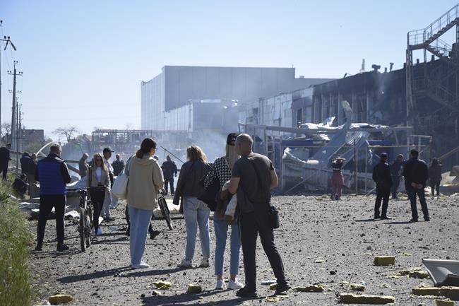 People stand near a destroyed building on the outskirts of Odesa, Ukraine, Tuesday, May 10, 2022. The Ukrainian military said Russian forces fired seven missiles a day earlier from the air at the crucial Black Sea port of Odesa, hitting a shopping center and a warehouse. (AP Photo/Max Pshybyshevsky)