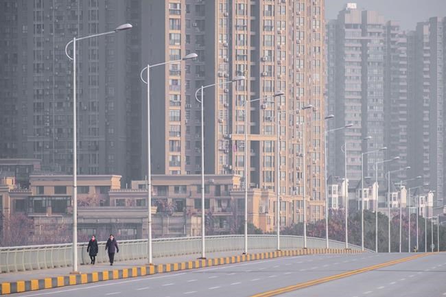 People wearing face masks walk down a deserted street in Wuhan in central China's Hubei Province, Tuesday, Jan. 28, 2020. China's death toll from a new viral disease that is causing mounting global concern rose by 25 to at least 106 on Tuesday as the United States and other governments prepared to fly their citizens out of the locked-down city at center of the outbreak. (AP Photo/Arek Rataj)