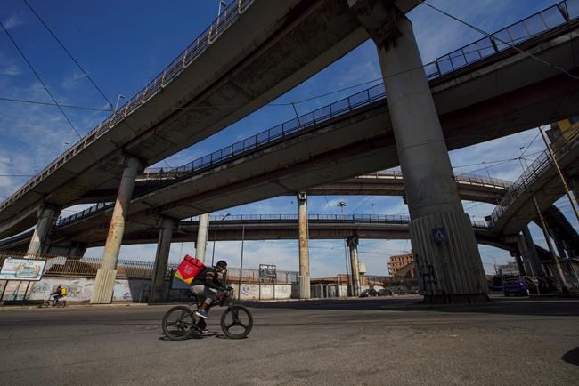 A food delivery person rides his bicycle in an empty street, in Rome, Wednesday, March 18, 2020. For most people, the new coronavirus causes only mild or moderate symptoms. For some it can cause more severe illness, especially in older adults and people with existing health problems.(AP Photo/Andrew Medichini)