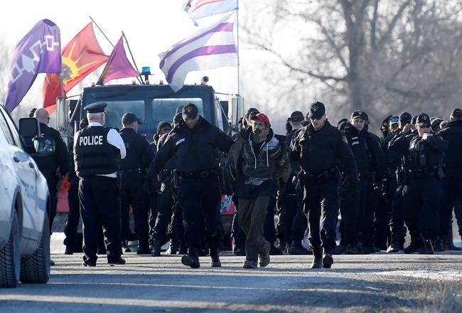 Ontario Provincial Police officers lead away a man after making an arrest at a rail blockade in Tyendinaga Mohawk Territory, near Belleville, Ont., on Monday Feb. 24, 2020, as they protest in solidarity with Wet'suwet'en Nation hereditary chiefs attempting to halt construction of a natural gas pipeline on their traditional territories. THE CANADIAN PRESS/Adrian Wyld