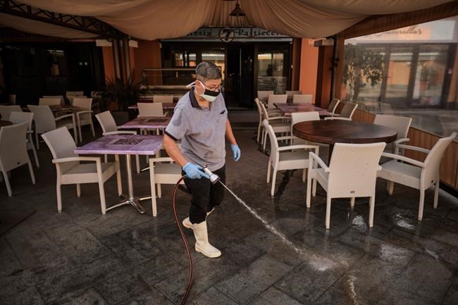 A staffer wearing a mask cleans the terrace of a shopping mall in La Caleta, in the Canary Island of Tenerife, Spain, Wednesday, Feb. 26, 2020. Worries over the ever-expanding economic fallout of the COVID-19 crisis multiplied, with factories idled, trade routes frozen and tourism crippled, while a growing list of countries braced for the illness to claim new territory. Even the Olympics, five months away, wasn't far enough off to keep people from wondering if it would go on as planned. (AP Photo)