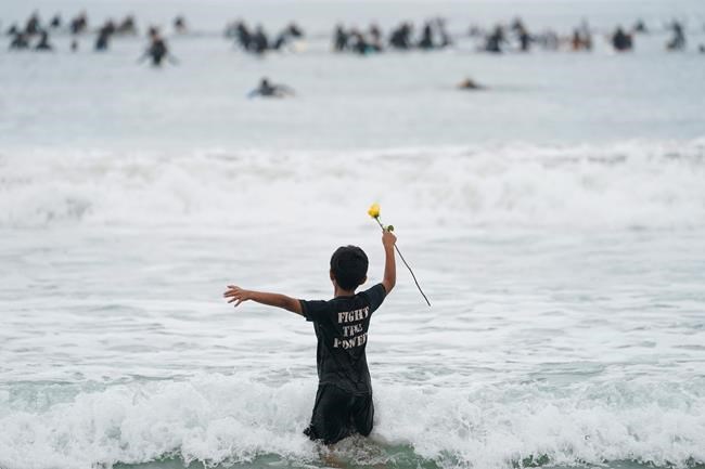 Nathan Rangel, 11, jumps in the water carrying a rose as surfers participate in a paddle out ceremony at