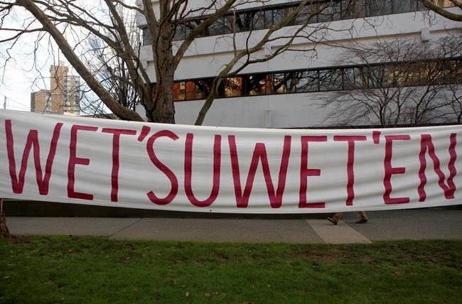 A person walks behind a banner as Wet'suwet'en supporters and Coastal GasLink opponents protest 20 government buildings throughout Victoria, Friday, Feb. 14, 2020. THE CANADIAN PRESS/Chad Hipolito