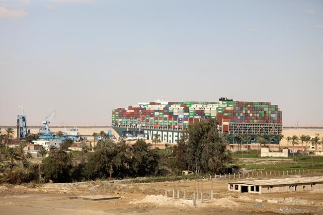 FILE - In this Sunday, March 28, 2021 file photo, the Ever Given, a Panama-flagged cargo ship wedged across the Suez Canal and blocking traffic looms over the village of Amer, near Suez, Egypt. The sleepy farming village of Amer overlooks the Suez Canal, one of the world’s most important waterways. Last week, it was suddenly thrust into the limelight after a massive container ship got stuck in the canal near the village. The contrast between tranquil village life and the busy artery of global shipping is stark. (AP Photo/Mohamed Elshahed, File)
