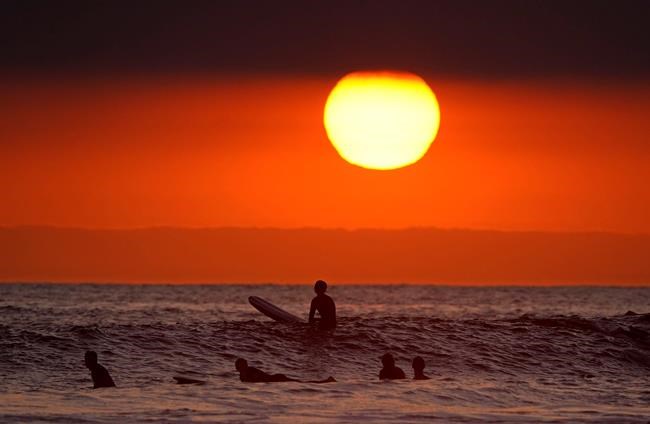 Surfers wait for waves as the sun goes down the day before the beach is scheduled to close during the coronavirus outbreak, Thursday, April 30, 2020, in Newport Beach, Calif. California Gov. Gavin Newsom on Thursday temporarily closed Orange County's coastline after large crowds were seen there. (AP Photo/Mark J. Terrill)