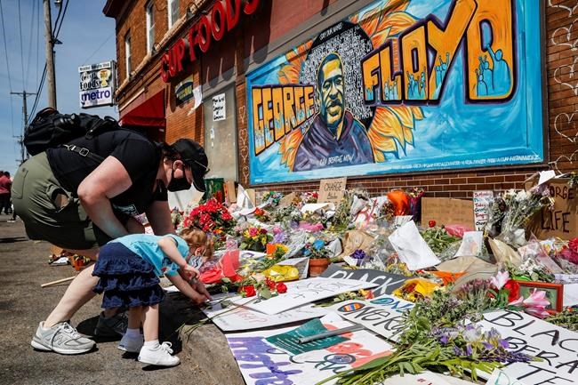 FILE - In this May 31, 2020 file photo, Jessica Knutson and her daughter Abigail, 3, place flowers at a memorial to George Floyd in Minneapolis. After a week of riots and looting over the loss of George Floyd, the Minneapolis black man who died after a police officer pressed his knee into his neck for more than eight minutes as he pleaded for air, parents are struggling to have the talk in this volatile moment, along with many others around race and racism. (AP Photo/John Minchillo, File)