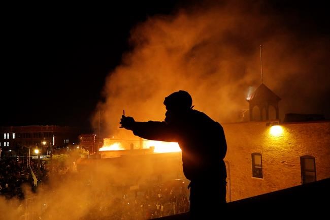 A man makes a video of protesters from the roof of the Minneapolis police 3rd Precinct building, Thursday, May 28, 2020, in Minneapolis. Protests over the death of George Floyd, a black man who died in police custody Monday, broke out in Minneapolis for a third straight night. (AP Photo/Julio Cortez)