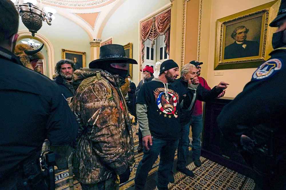 Protesters walk as U.S. Capitol Police officers watch in a hallway near the Senate chamber at the Capitol in Washington, Wednesday, Jan. 6, 2021, near the Ohio Clock. (AP Photo/Manuel Balce Ceneta)