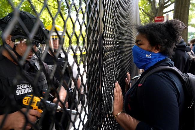 A demonstrator watches as a U.S. Secret Service police office works on a fence blocking Lafayette Park as protests in the death of George Floyd continue, Tuesday, June 2, 2020, near the White House in Washington. Floyd died after being restrained by Minneapolis police officers. (AP Photo/Evan Vucci)