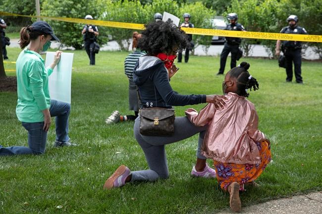 Ericka Ward-Audena, of Washington, puts her hand on her daughter Elle Ward-Audena, 7, as they take a knee in front of a police line during a protest of President Donald Trump's visit to the Saint John Paul II National Shrine, Tuesday, June 2, 2020, in Washington.
