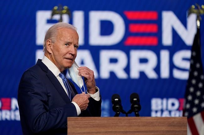 Democratic presidential candidate former Vice President Joe Biden removes his face mask as he arrives to speak, Friday, Nov. 6, 2020, in Wilmington, Del. (AP Photo/Carolyn Kaster)