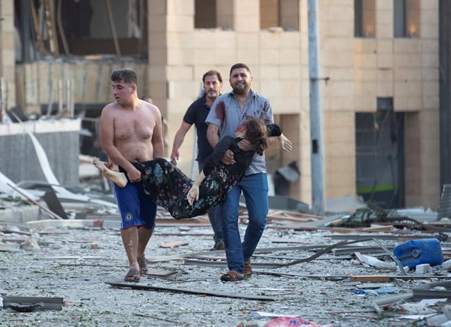 People evacuate wounded after of a massive explosion in Beirut, Lebanon, Tuesday, Aug. 4, 2020. Massive explosions rocked downtown Beirut on Tuesday, flattening much of the port, damaging buildings and blowing out windows and doors as a giant mushroom cloud rose above the capital. Witnesses saw many people injured by flying glass and debris. (AP Photo/Hassan Ammar)