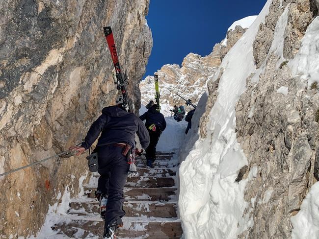 Skiers make their way to reach the start of the men's downhill course, at the alpine ski World Championships in Cortina d'Ampezzo, Italy, Friday, Feb. 12, 2021. To reach the start of the new men's downhill course in Cortina, skiers have to climb 223 steps at an altitude of 2,400 meters (8,000 feet). The course's name, Vertigine, translates to
