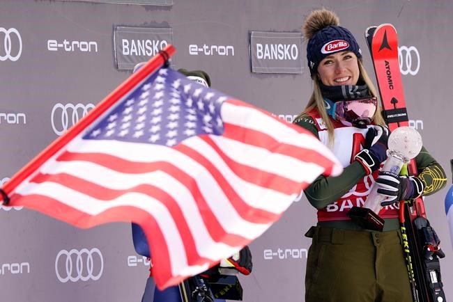 United States' Mikaela Shiffrin is fried by a US flag as she smiles on the podium after winning an alpine ski, women's World Cup super-G, in Bansko, Bulgaria, Sunday, Jan. 26, 2020. (AP Photo/Giovanni Auletta)