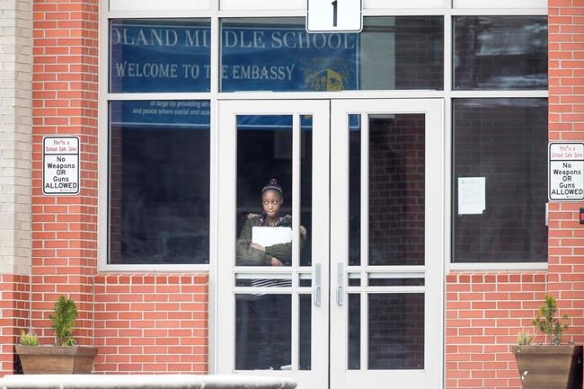 A student waits at the front entrance at Woodland Middle School in East Point, Ga.,Monday, March 9, 2020. The Fulton County School system has decided to close schools on Tuesday after a teacher tested positive with the coronavirus. The teacher was at Woodland Middle school on Friday. (Alyssa Pointer/Atlanta Journal-Constitution via AP)