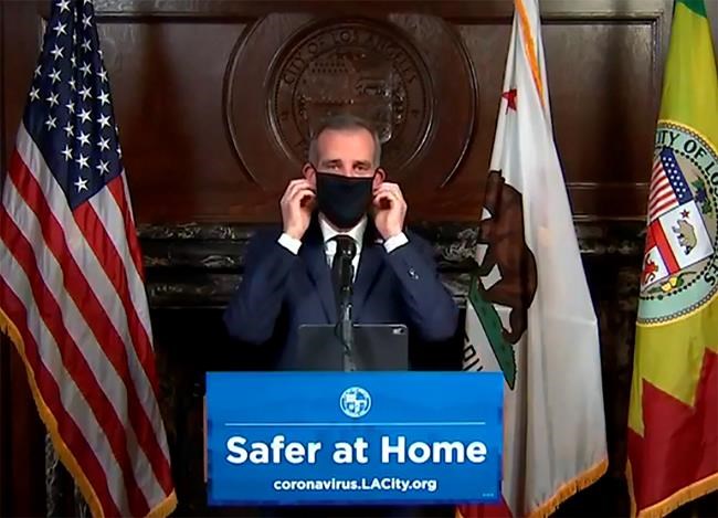 This still image taken from a live stream provided by Office of Mayor Eric Garcetti showing Los Angeles Mayor Garcetti displaying putting on a protective face mask during his daily news conference in Los Angeles on Wednesday, April 1, 2020. Garcetti has recommended that the city's 4 million people wear masks when going outside amid the spreading coronavirus. (Office of Mayor Eric Garcetti via AP)