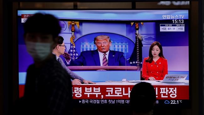 A man wearing a face mask walks near a TV screen reporting about U.S. President Donald Trump and first lady Melania Trump during a news program with a file image of Trump at the Seoul Railway Station in Seoul, South Korea, Friday, Oct. 2, 2020. Trump said early Friday that he and Melania Trump have tested positive for the coronavirus, a stunning announcement that plunges the country deeper into uncertainty just a month before the presidential election. The Korean letters read: