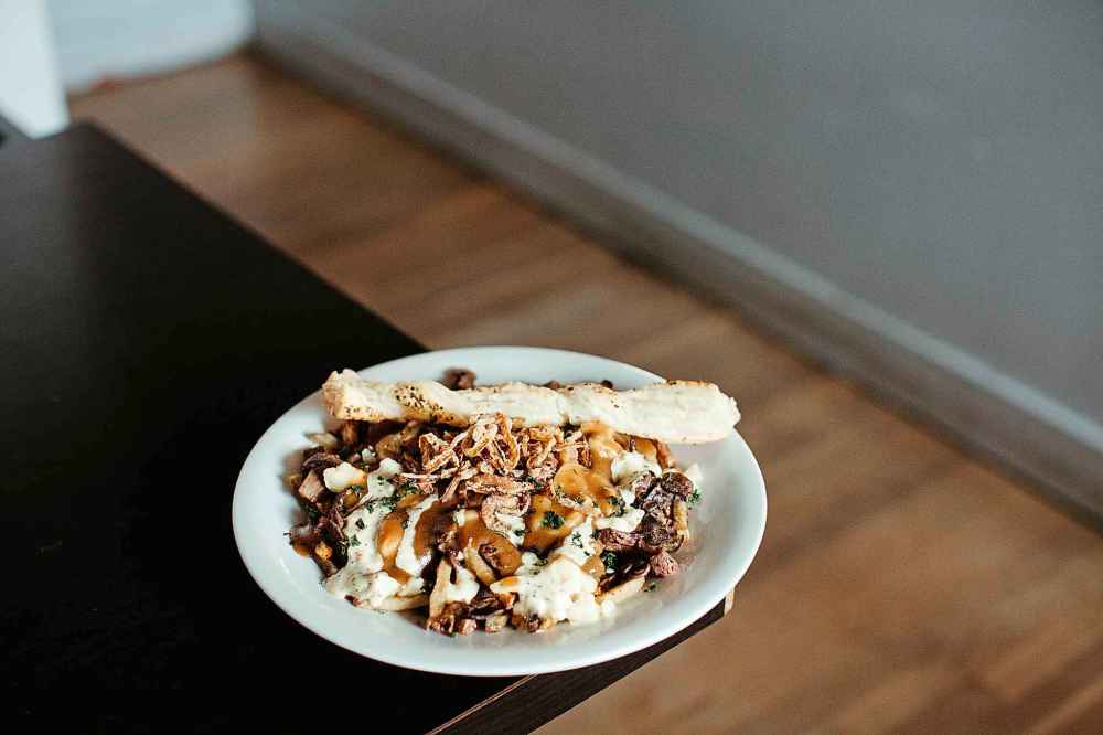 The Wellington at Le Garage features shoestring fries with red wine-braised beef, horseradish aioli drizzle, cheese curds, sautéed mushrooms, crispy fried onions, and a puff pastry twist, topped with house gravy.