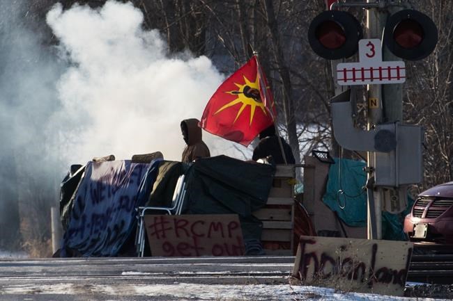 A protesters stand beside smoke at the closed train tracks in Tyendinaga Mohawk Territory near Belleville, Ont., on Thursday Feb. 20, 2020, as they protest in solidarity with the Wet'suwet'en hereditary chiefs opposed to the LNG pipeline in northern British Columbia. THE CANADIAN PRESS/Lars Hagberg