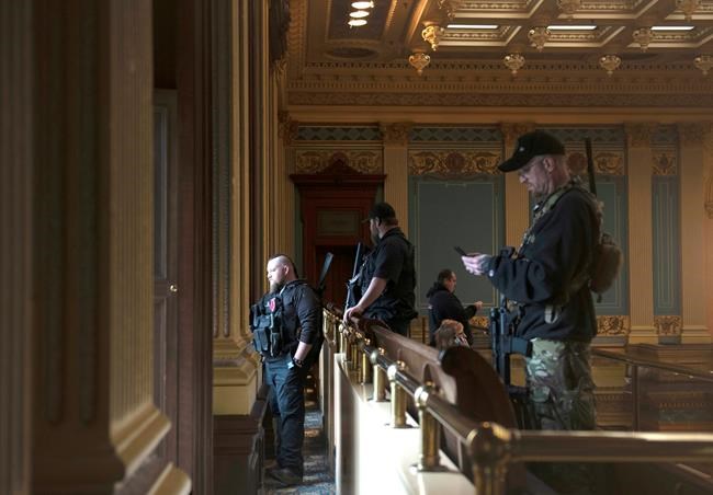 FILE - In this April 30, 2020, file photo, armed members of a militia group watch the protest outside while waiting for the Michigan Senate to vote at the Capitol in Lansing, Mich. Michigan has banned the open carry of guns in the state Capitol a week after an armed mob rioted in the U.S. Capitol and following an attempt to storm the statehouse last year. (Nicole Hester/MLive.com/Ann Arbor News via AP File)