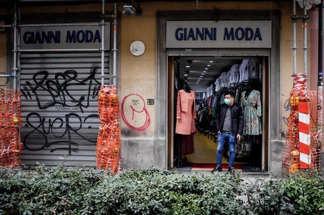 A man wearing a face masks stands at the entrance of his shop in downtown Milan's Chinese neighborhood Wednesday, Feb. 26, 2020. The viral outbreak that began in China and has infected more than 80,000 people globally, so far caused 374 cases and 12 deaths in Italy, according to the last figures released by civil protection. (Claudio Furlan/LaPresse via AP)
