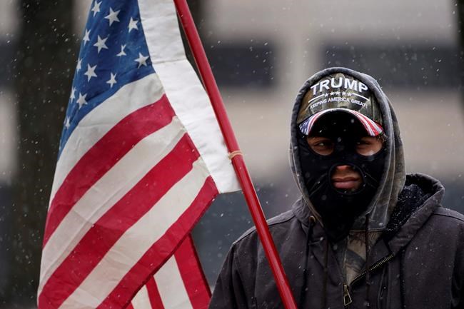 A man stands outside the state capitol wearing a Trump hat with an American flag in Lansing, Mich., Sunday, Jan. 17, 2021. (AP Photo/Paul Sancya)