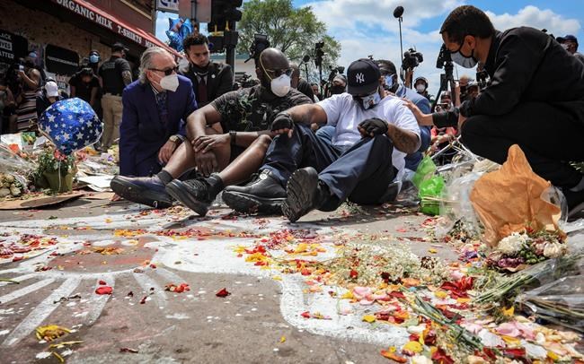 An emotional Terrence Floyd, second from right, is comforted as he sits at the spot at the intersection of 38th Street and Chicago Avenue, Minneapolis, Minn., where his brother George Floyd, encountered police and died while in their custody, Monday, June 1, 2020. (AP Photo/Bebeto Matthews)